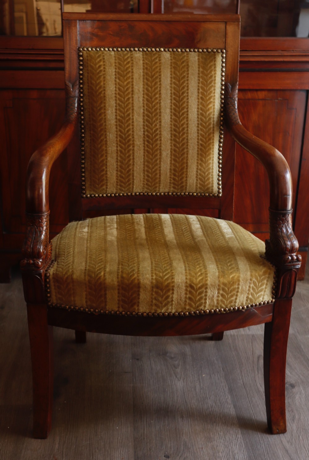 An antique carved mahogany armchair featuring striped velvet upholstery, swept arms with detailed carvings, and brass stud trim. View II