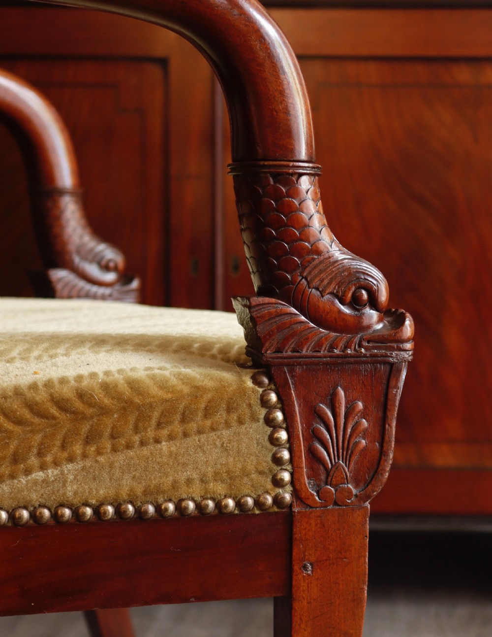 An antique carved mahogany armchair featuring striped velvet upholstery, swept arms with detailed carvings, and brass stud trim. View V