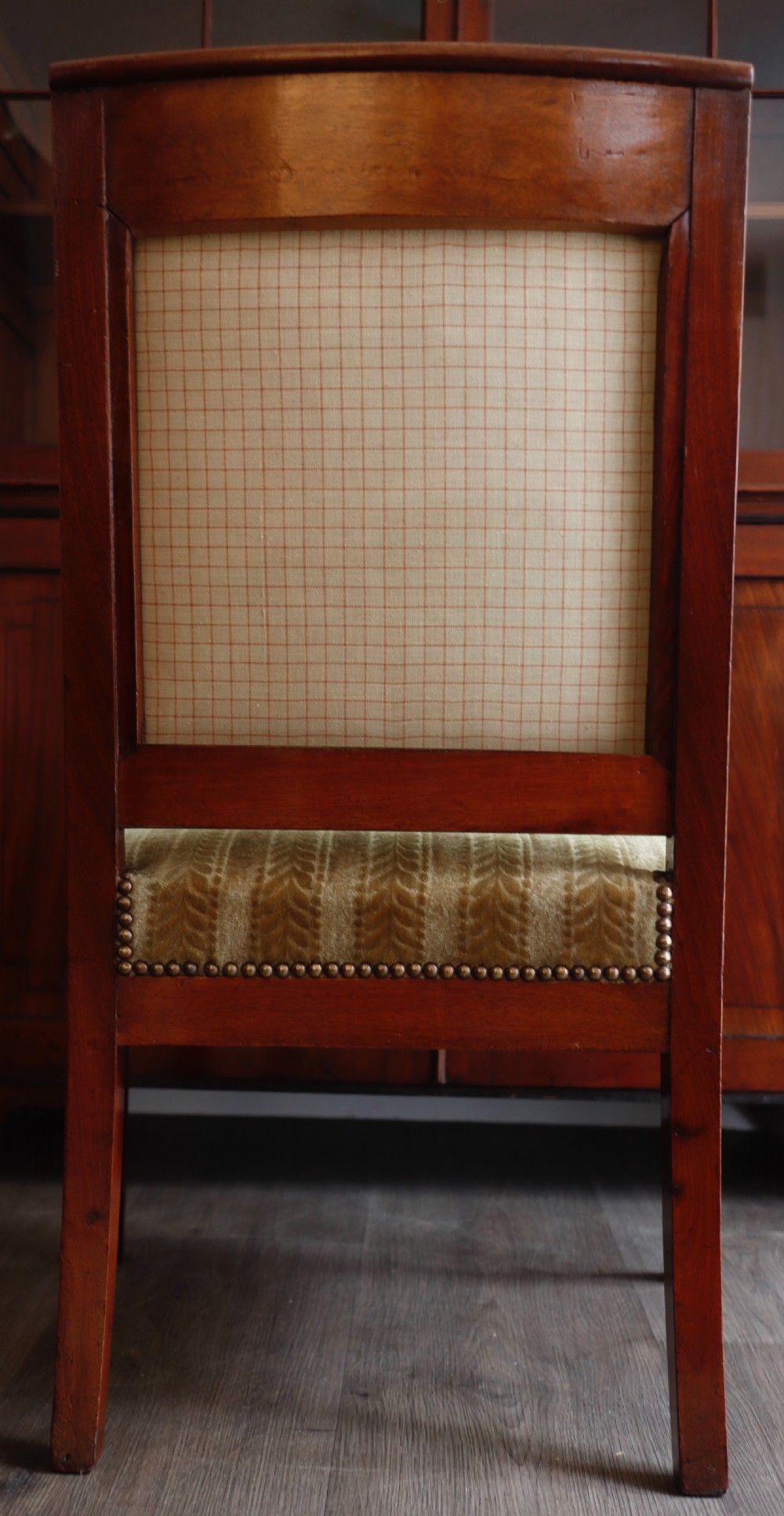 An antique carved mahogany armchair featuring striped velvet upholstery, swept arms with detailed carvings, and brass stud trim. View VI