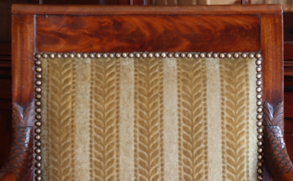 An antique carved mahogany armchair featuring striped velvet upholstery, swept arms with detailed carvings, and brass stud trim. View VII