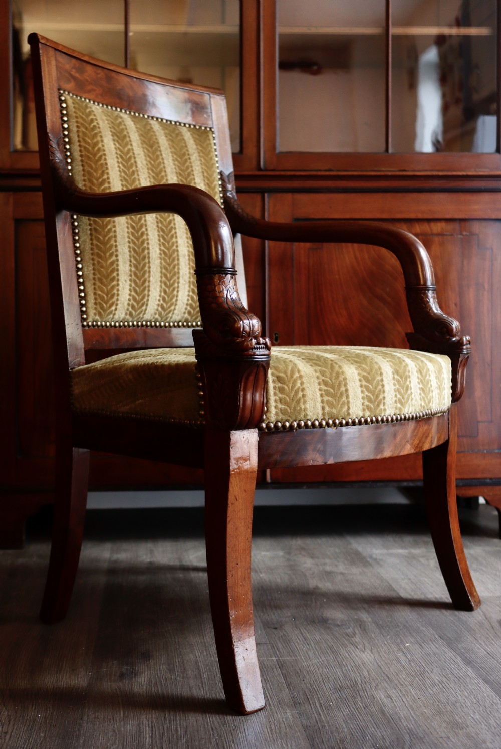 An antique carved mahogany armchair featuring striped velvet upholstery, swept arms with detailed carvings, and brass stud trim. View III