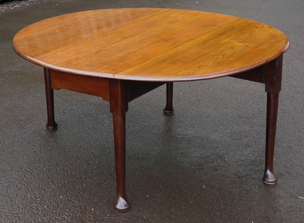 An 18th-century Georgian mahogany oval drop-leaf table resting on turned tapered legs with pad feet.