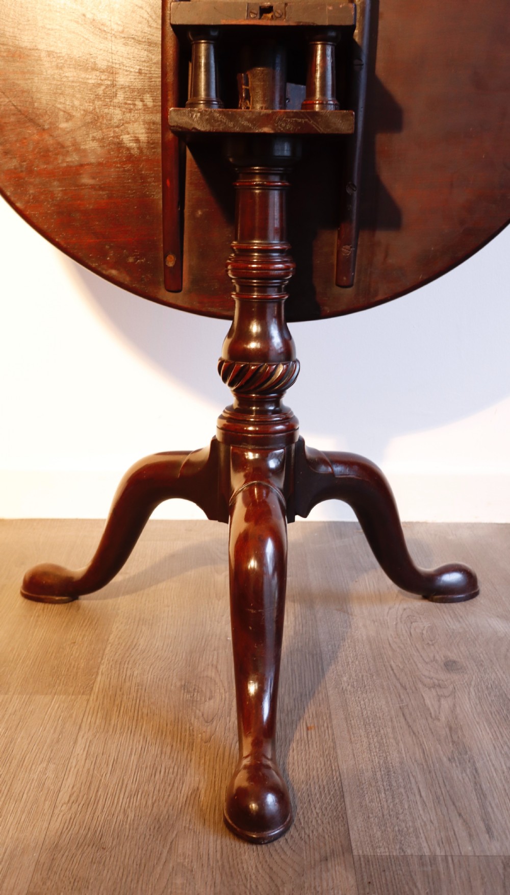A circular mahogany tilt-top table shown with its surface flipped vertically, resting on a turned column with three pad-foot cabriole legs. View III