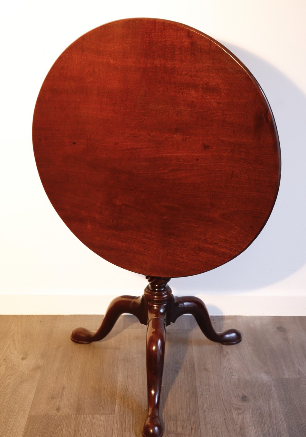 A circular mahogany tilt-top table shown with its surface flipped vertically, resting on a turned column with three pad-foot cabriole legs.