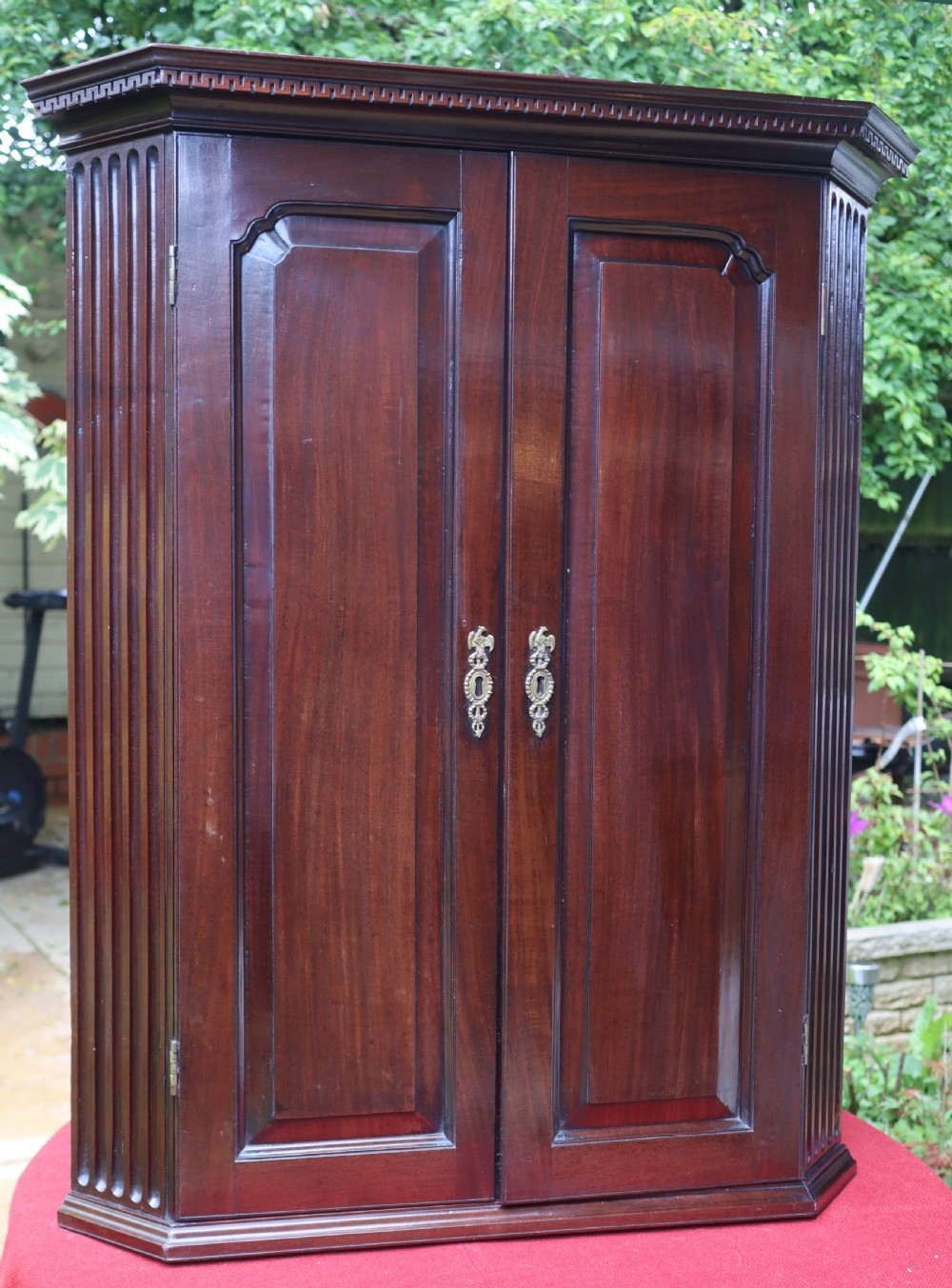 An 18th-century Georgian mahogany two-door corner cupboard featuring fluted pilasters, dentil moulding along the top cornice, and shaped fielded panel doors with brass escutcheons.