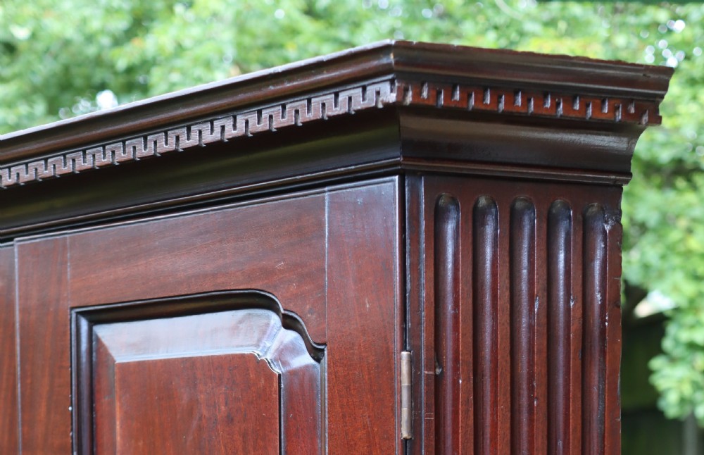 An 18th-century Georgian mahogany two-door corner cupboard featuring fluted pilasters, dentil moulding along the top cornice, and shaped fielded panel doors with brass escutcheons. View II