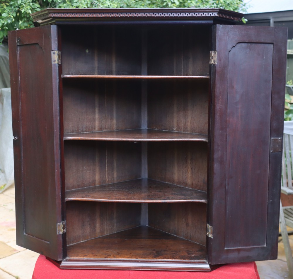 An 18th-century Georgian mahogany two-door corner cupboard featuring fluted pilasters, dentil moulding along the top cornice, and shaped fielded panel doors with brass escutcheons. View VI
