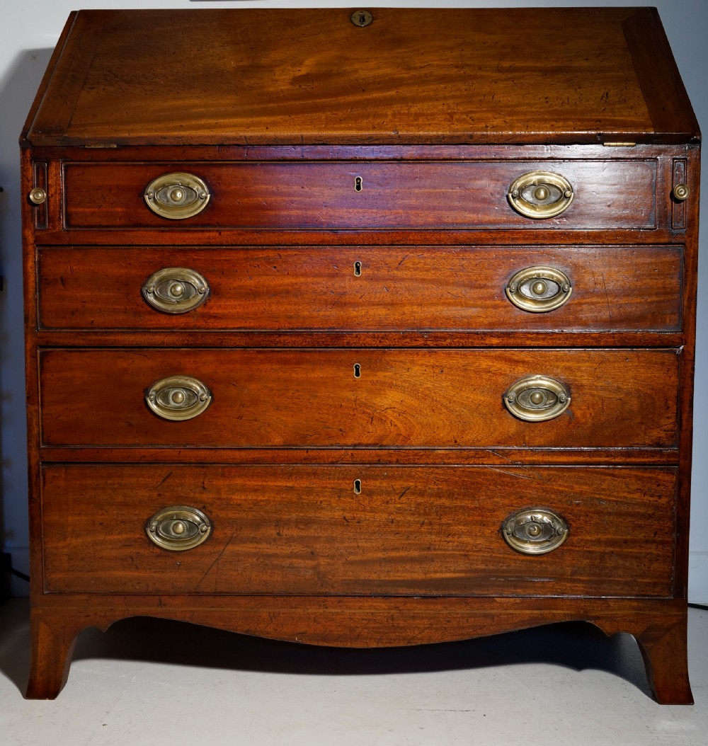 An antique Georgian mahogany bureau featuring a slant-front writing slope over four graduated drawers with brass oval handles.