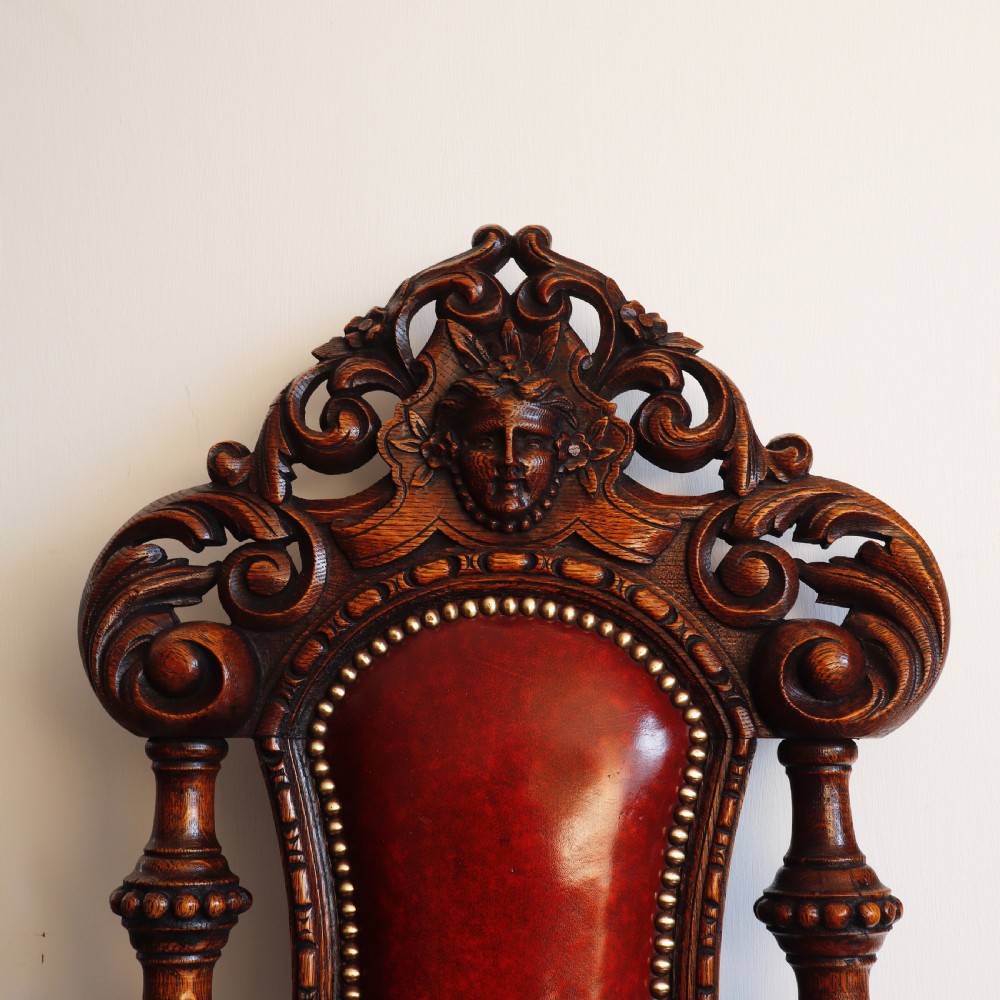 A pair of Victorian carved oak side chairs featuring red leather studded upholstery, carved cresting, and turned front legs on casters. View III