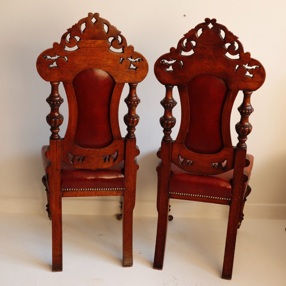 A pair of Victorian carved oak side chairs featuring red leather studded upholstery, carved cresting, and turned front legs on casters. View VI