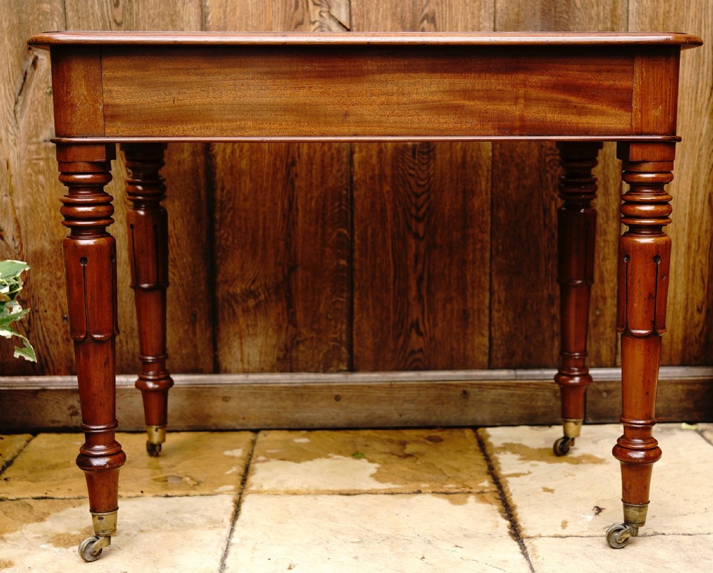A rectangular mahogany centre table featuring a polished top surface, turned legs, and brass castors. View IV