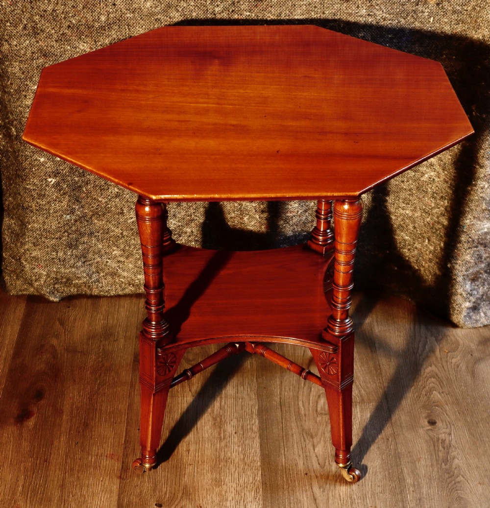 An antique octagonal walnut occasional table featuring a lower tier shelf, turned legs, rosette carving, cross-stick bracing, and brass castors.