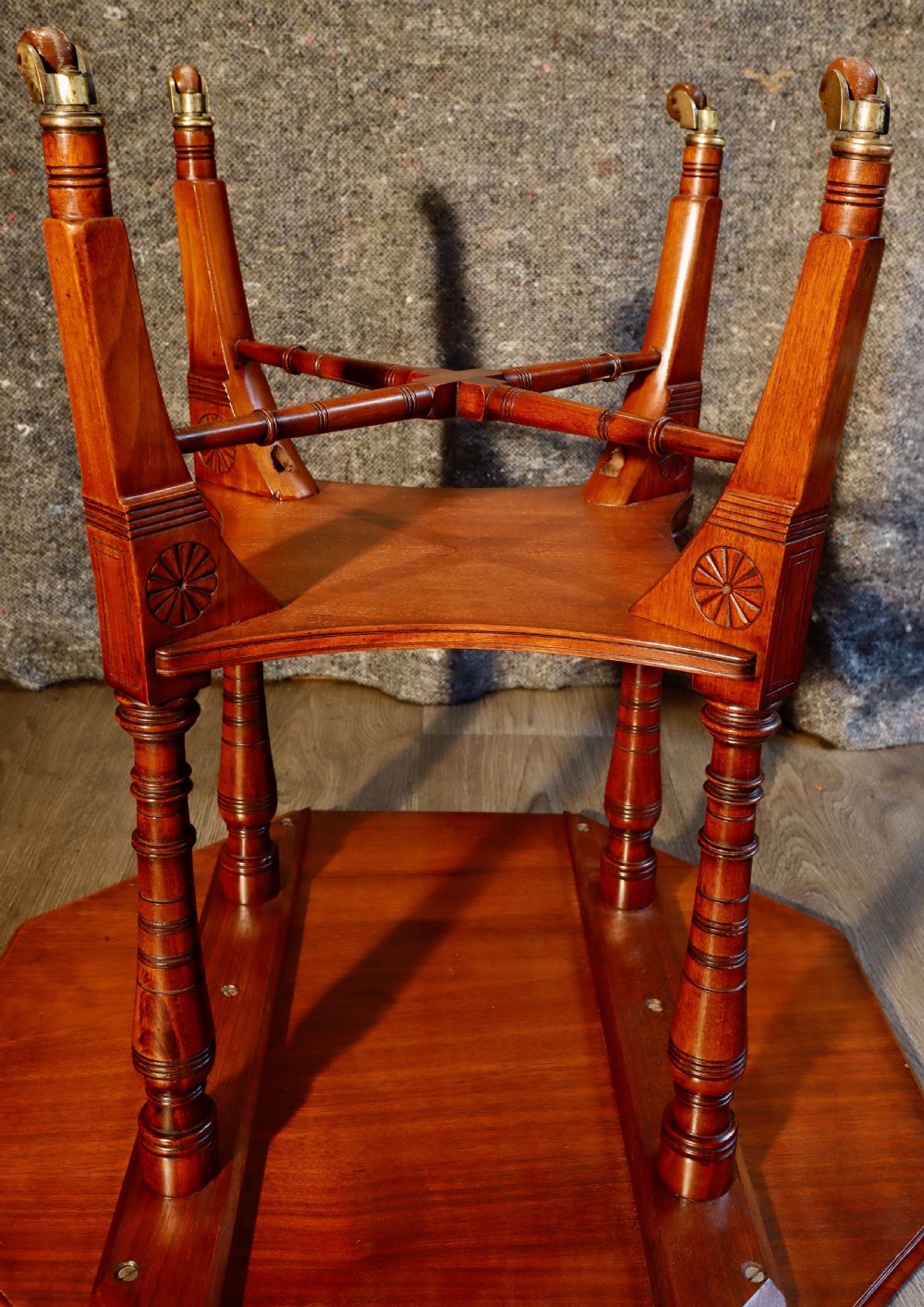 An antique octagonal walnut occasional table featuring a lower tier shelf, turned legs, rosette carving, cross-stick bracing, and brass castors. View V
