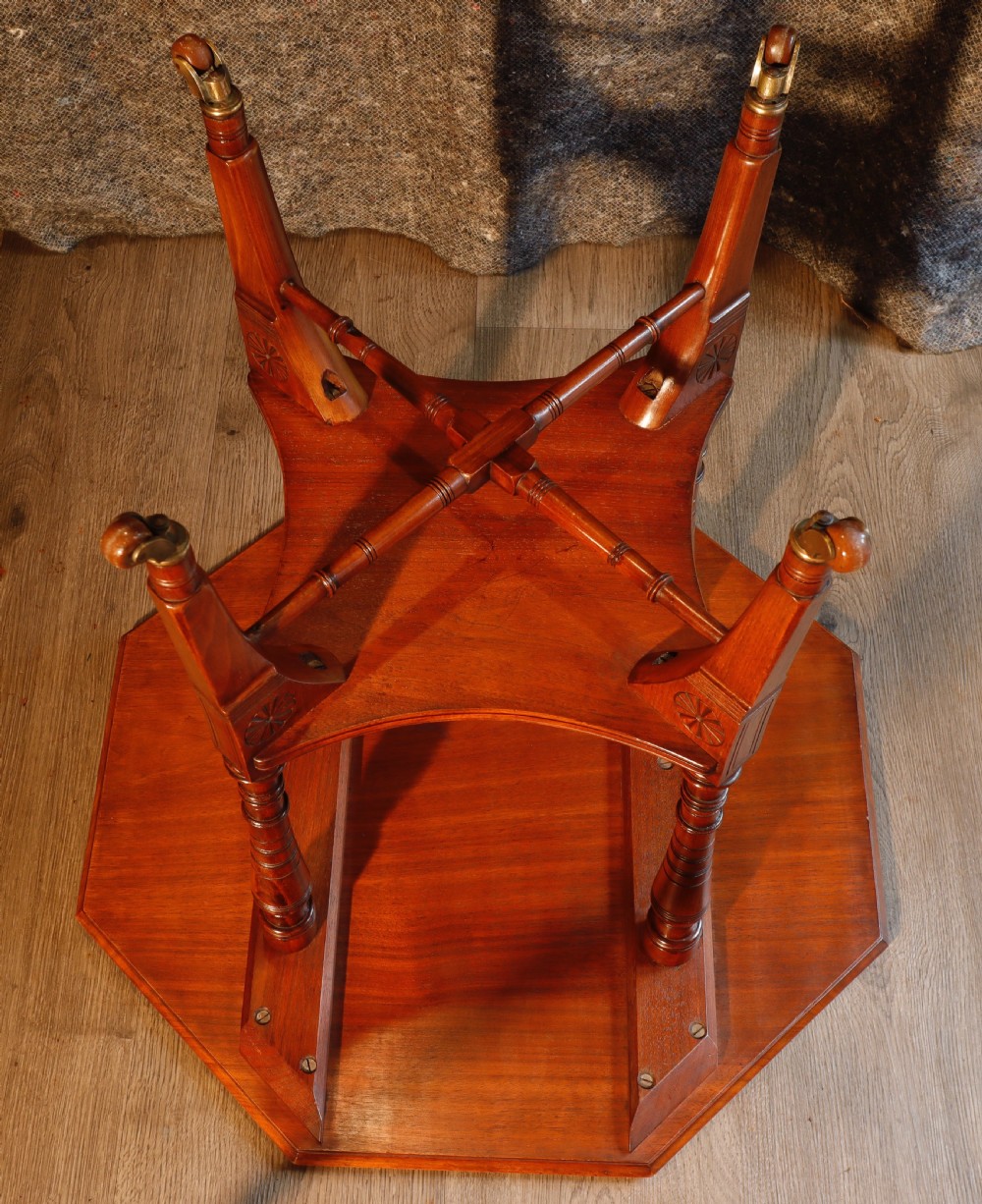 An antique octagonal walnut occasional table featuring a lower tier shelf, turned legs, rosette carving, cross-stick bracing, and brass castors. View VI