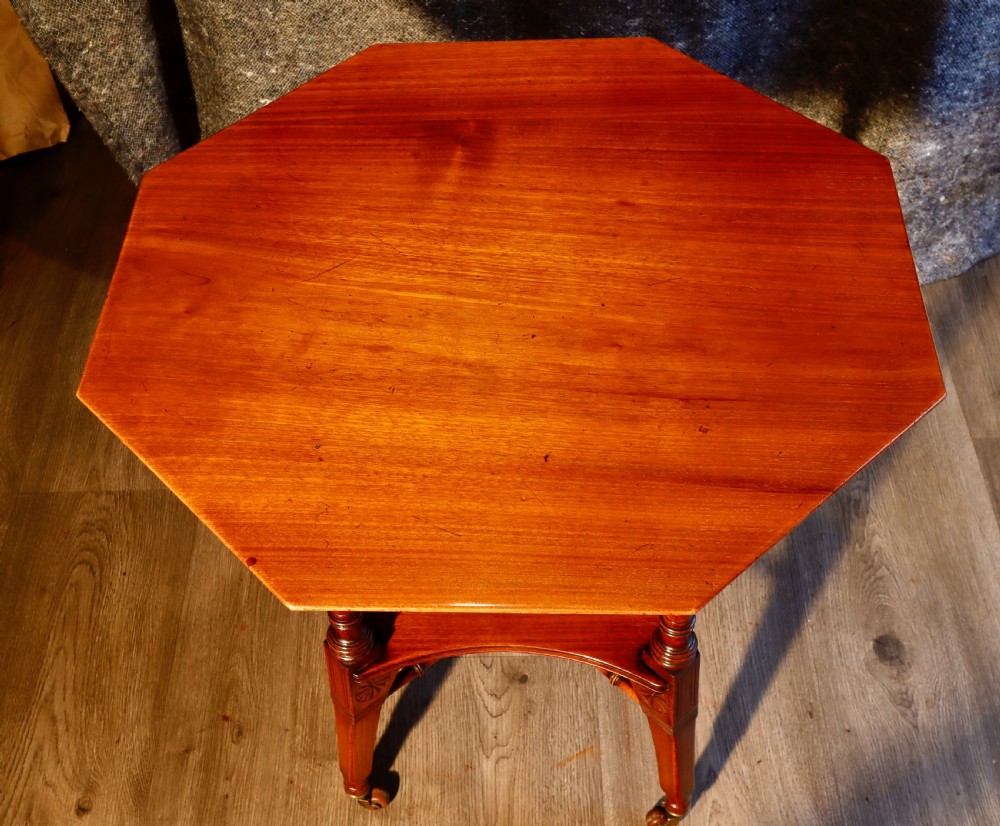 An antique octagonal walnut occasional table featuring a lower tier shelf, turned legs, rosette carving, cross-stick bracing, and brass castors. View VII