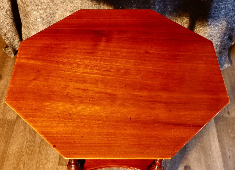 An antique octagonal walnut occasional table featuring a lower tier shelf, turned legs, rosette carving, cross-stick bracing, and brass castors. View VIII