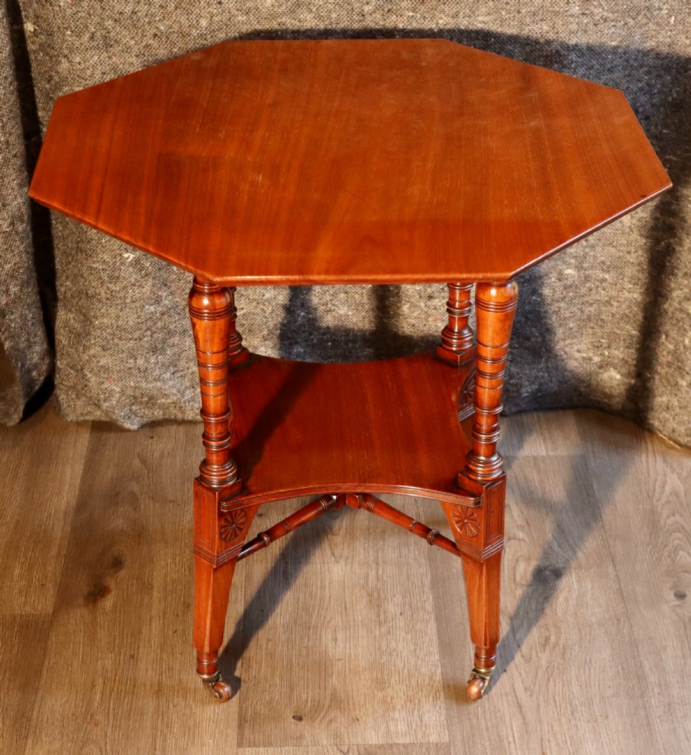 An antique octagonal walnut occasional table featuring a lower tier shelf, turned legs, rosette carving, cross-stick bracing, and brass castors. View IX