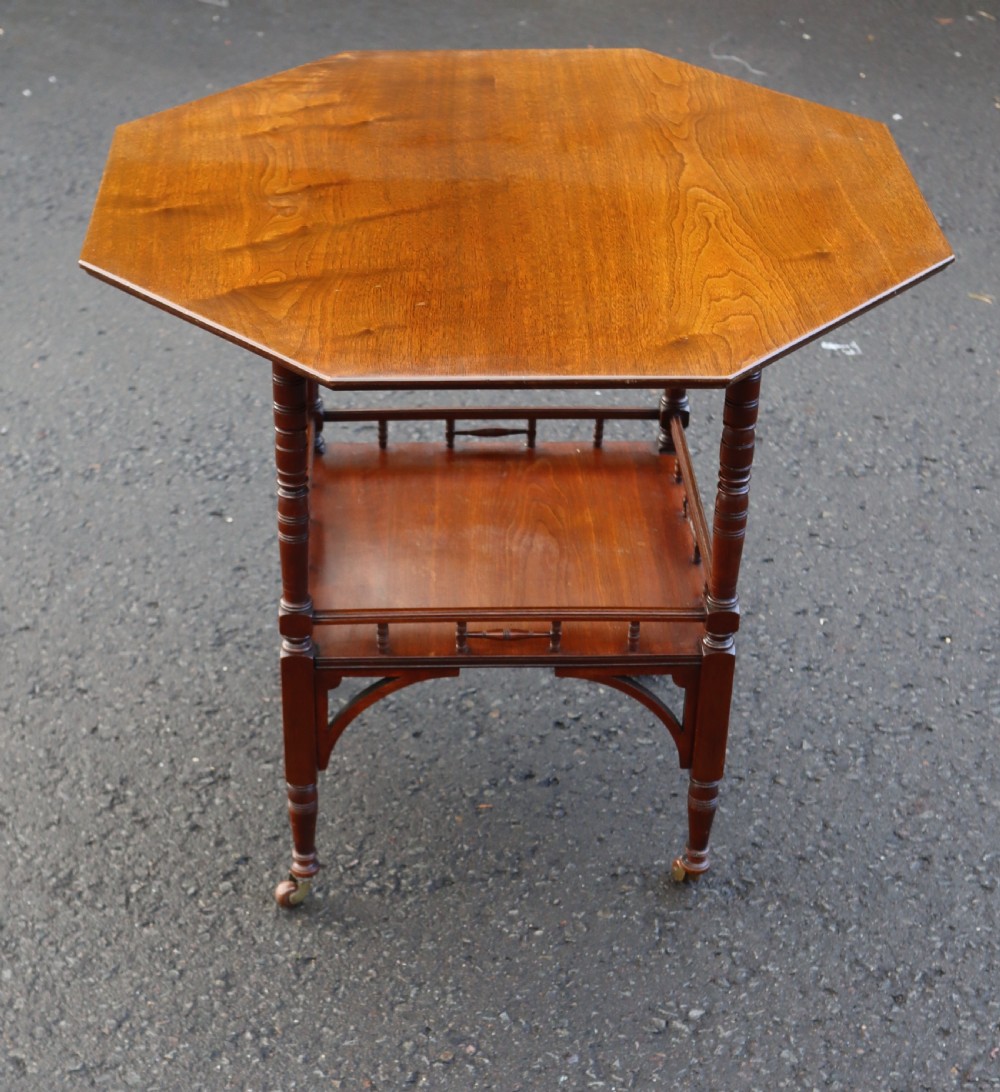 A late Victorian octagonal walnut occasional table featuring a secondary lower tier with a spindle gallery, turned legs, and brass castors.