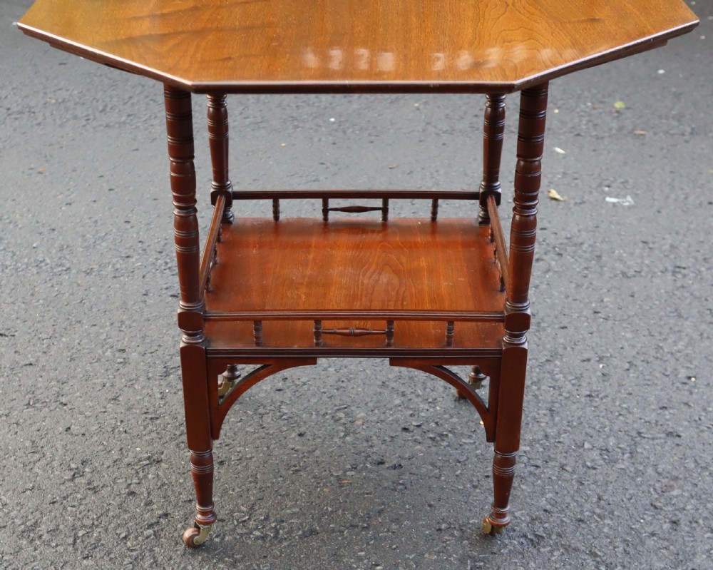 A late Victorian octagonal walnut occasional table featuring a secondary lower tier with a spindle gallery, turned legs, and brass castors. View V