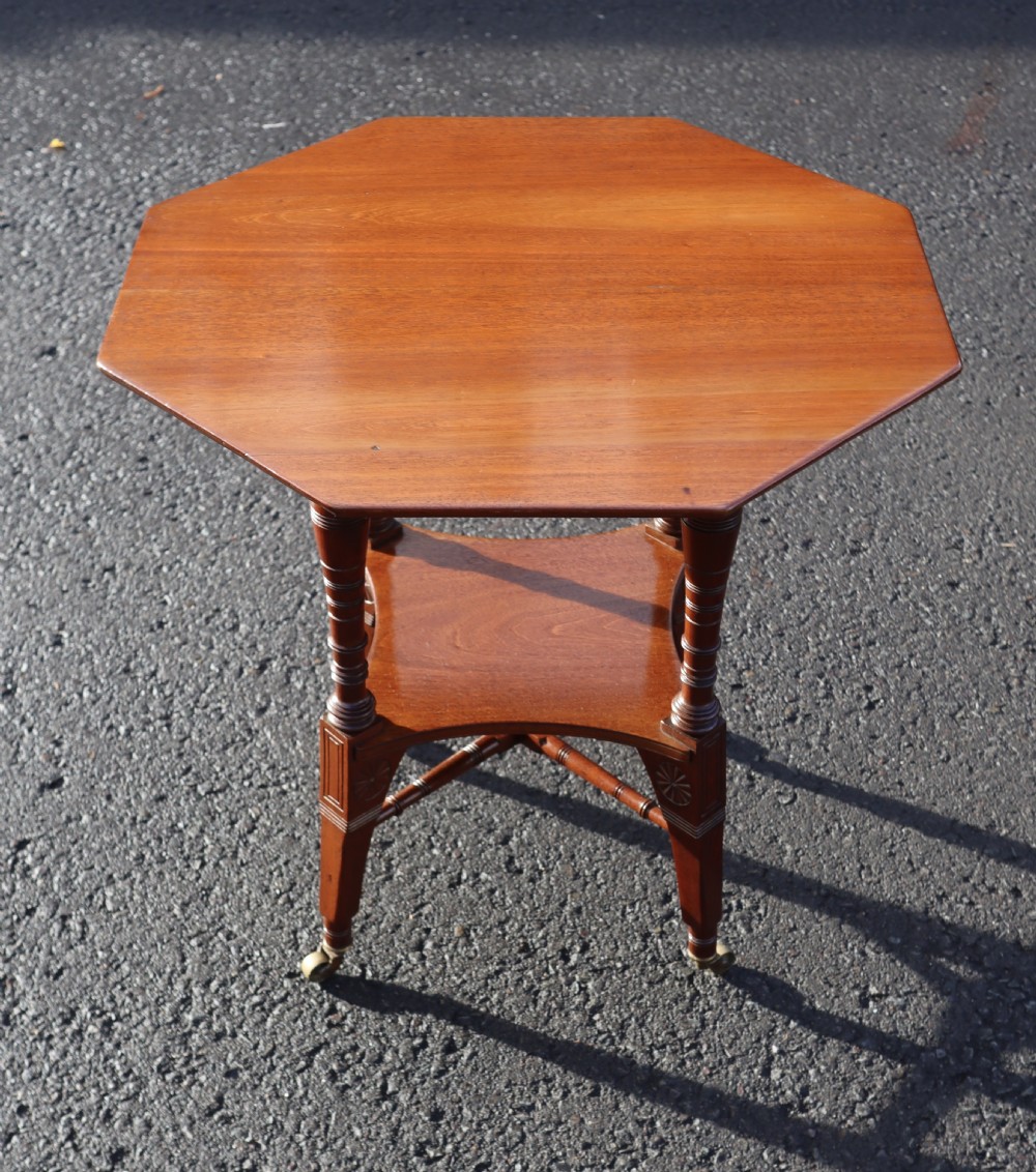 An antique walnut two-tier occasional table featuring an octagonal top, turned support legs, lower tier, and brass castors.