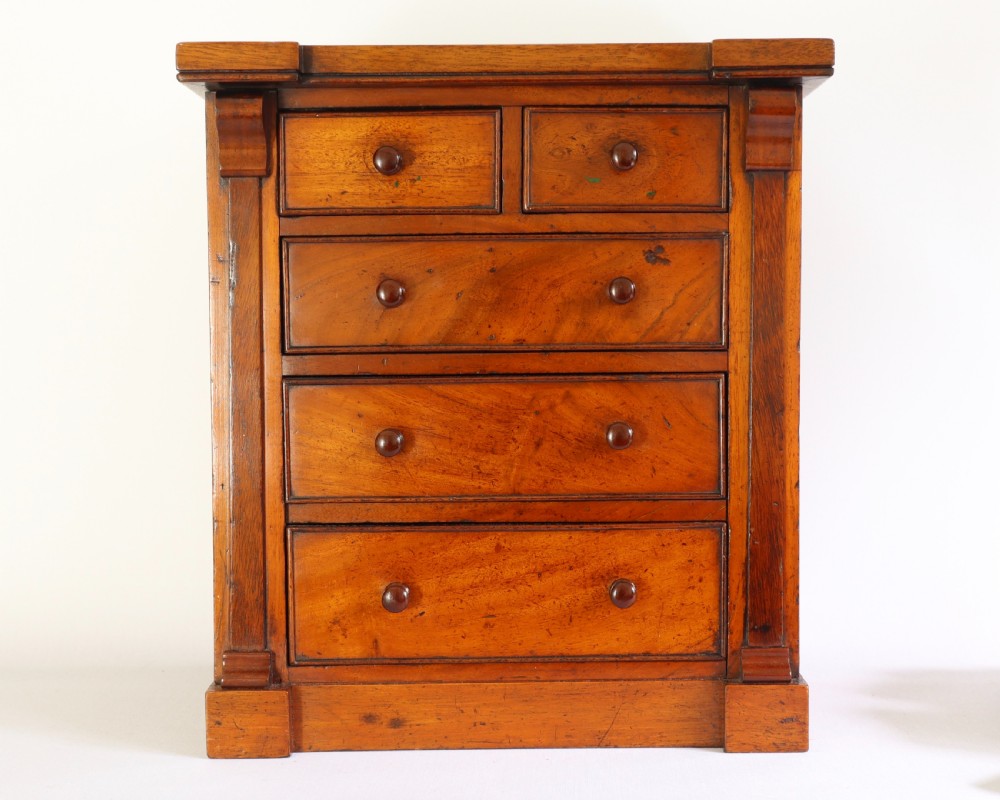 A Victorian mahogany miniature chest of drawers featuring two short over three long drawers with turned wooden knobs and side pilasters.