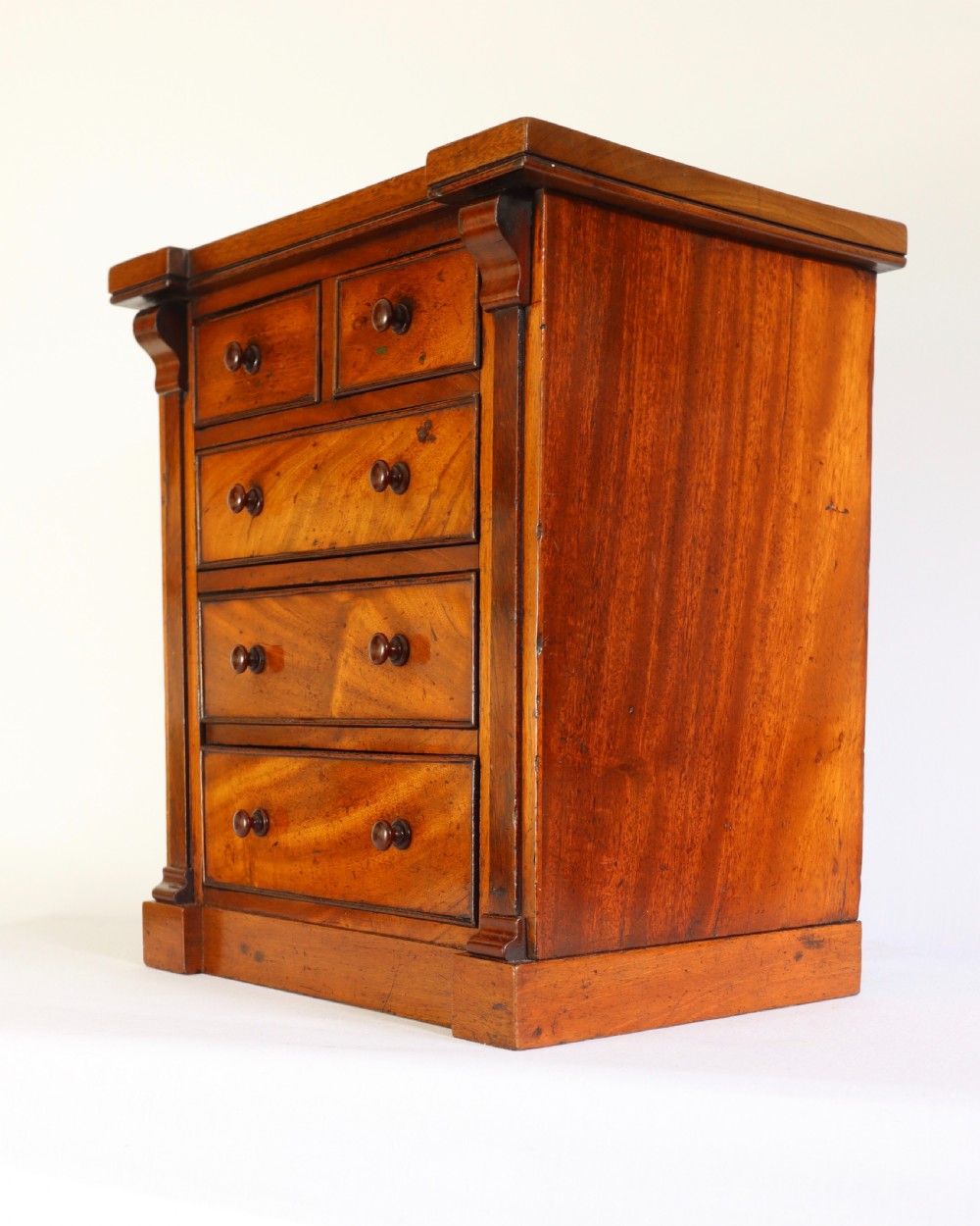 A Victorian mahogany miniature chest of drawers featuring two short over three long drawers with turned wooden knobs and side pilasters. View II