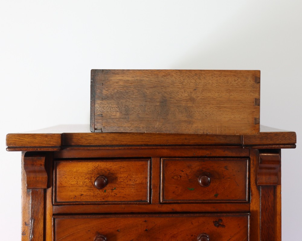 A Victorian mahogany miniature chest of drawers featuring two short over three long drawers with turned wooden knobs and side pilasters. View V