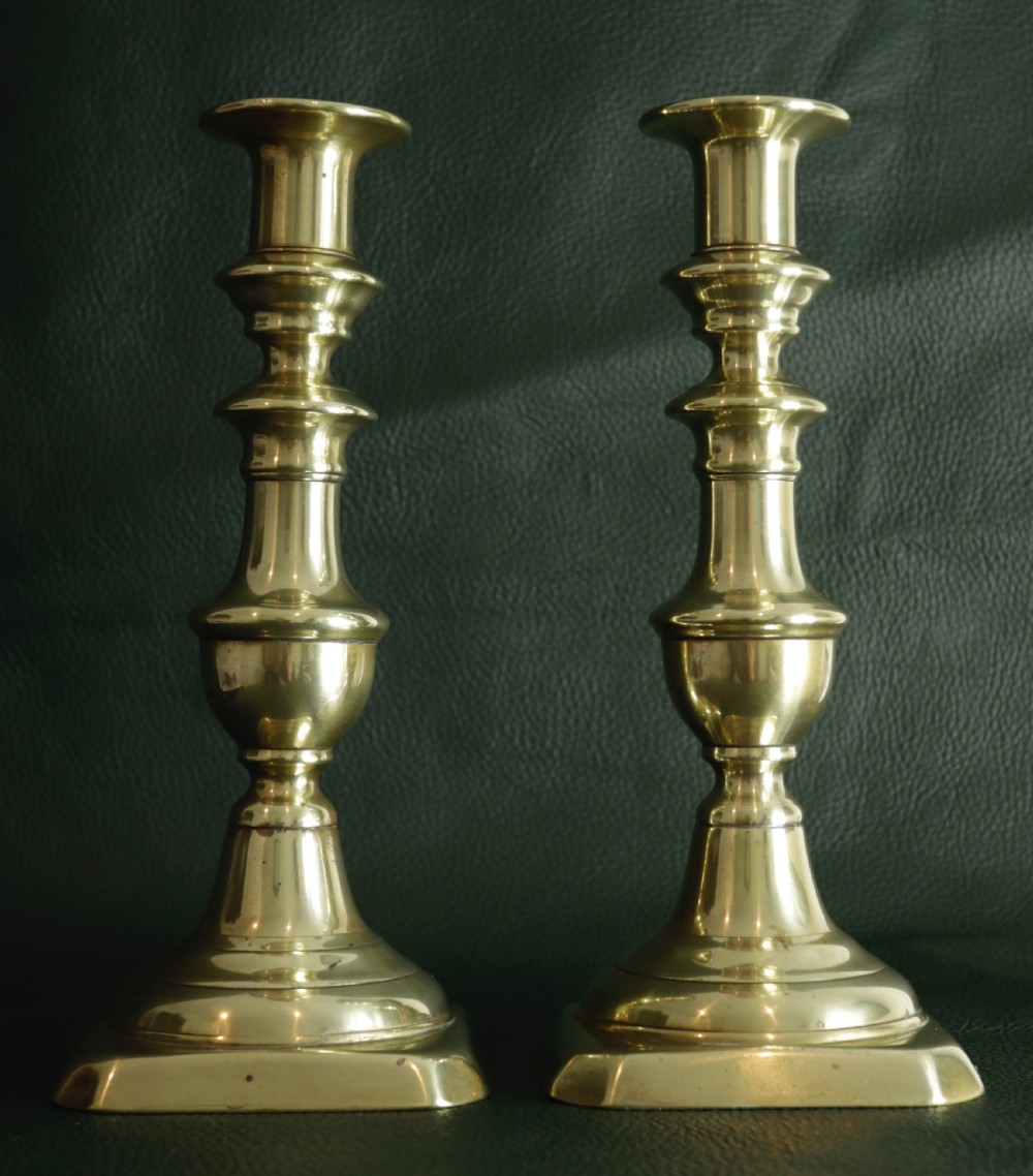 A pair of turned brass candlesticks featuring vase-shaped columns and square stepped bases.