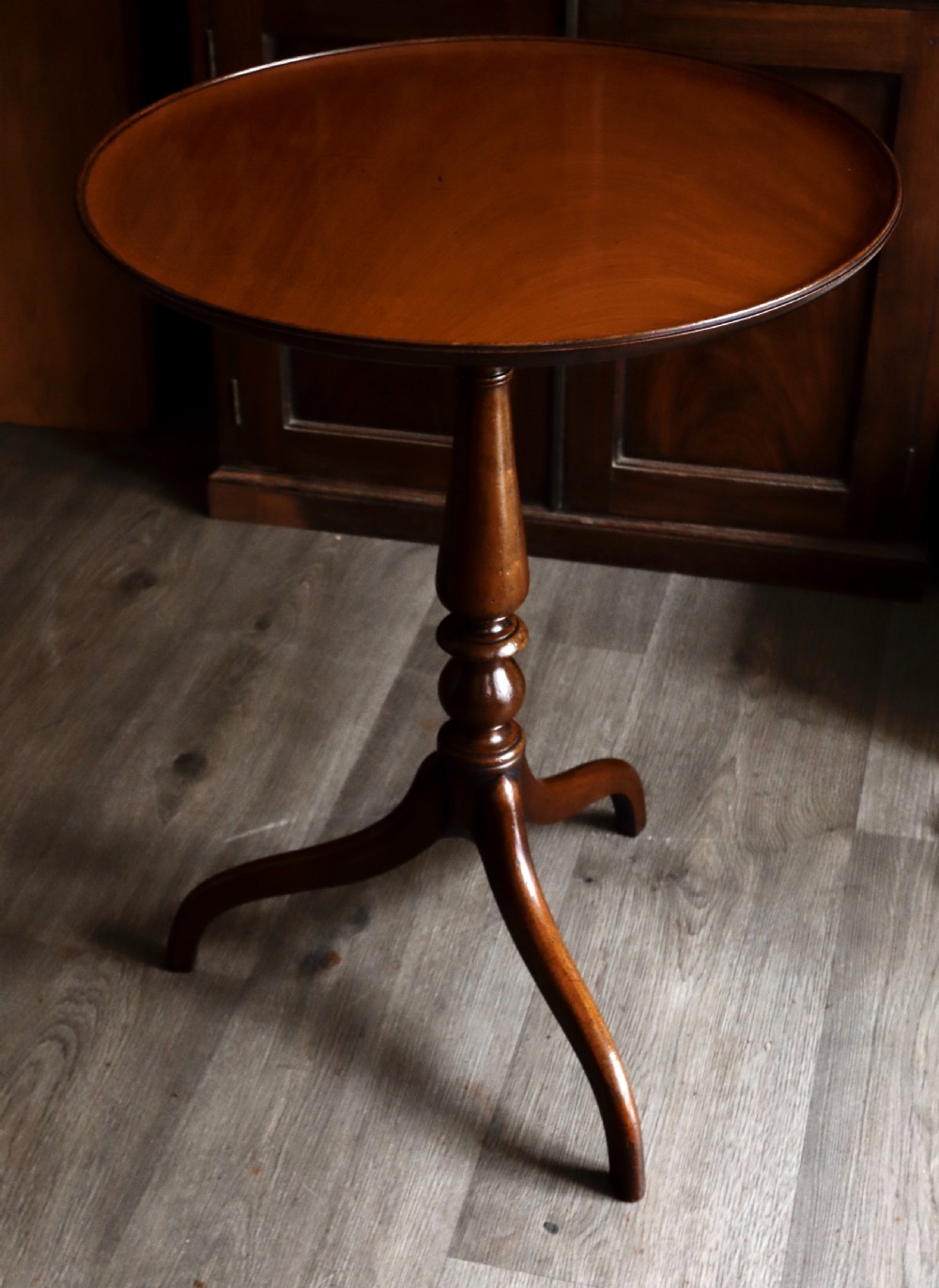 A polished mahogany tripod table with a circular top, turned central column, and three curved legs.
