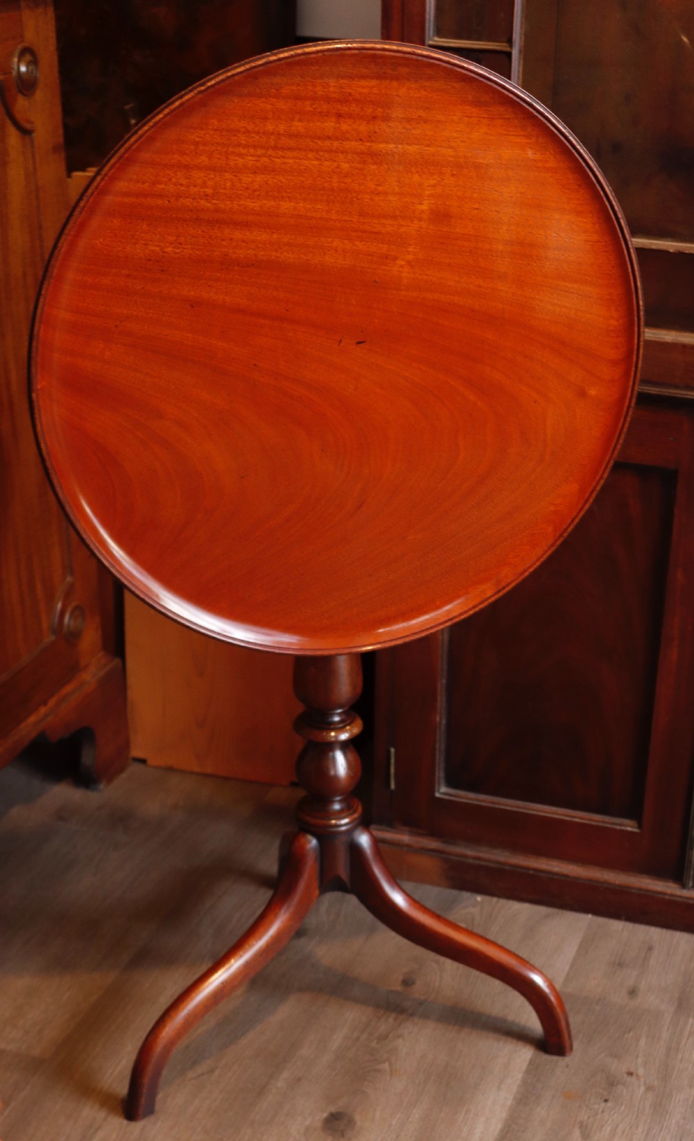 A polished mahogany tripod table with a circular top, turned central column, and three curved legs. View VII