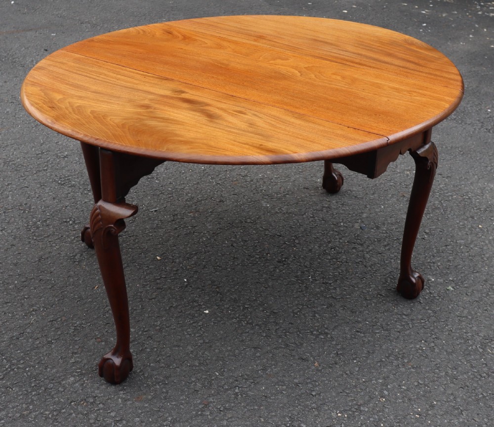 An antique mahogany drop-leaf dining table featuring carved cabriole legs terminating in claw and ball feet.