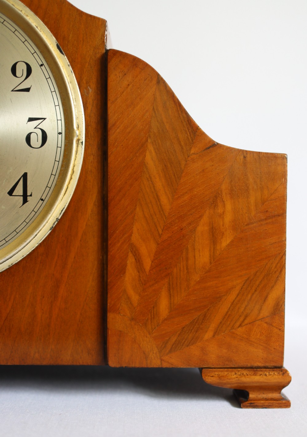An Art Deco wooden mantel clock featuring an arched case with book-matched veneer and a round silvered dial with Arabic numerals. View II