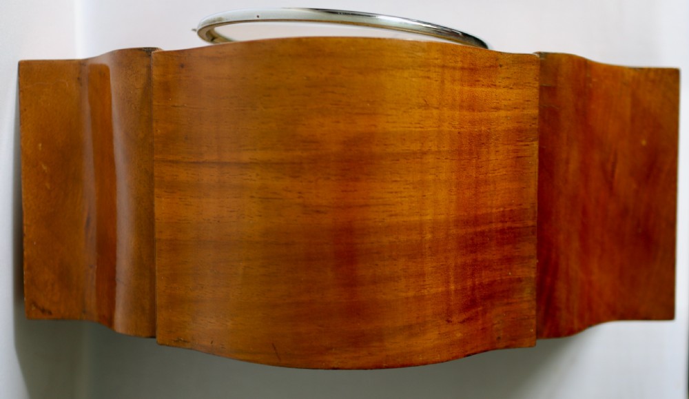 An Art Deco wooden mantel clock featuring an arched case with book-matched veneer and a round silvered dial with Arabic numerals. View III