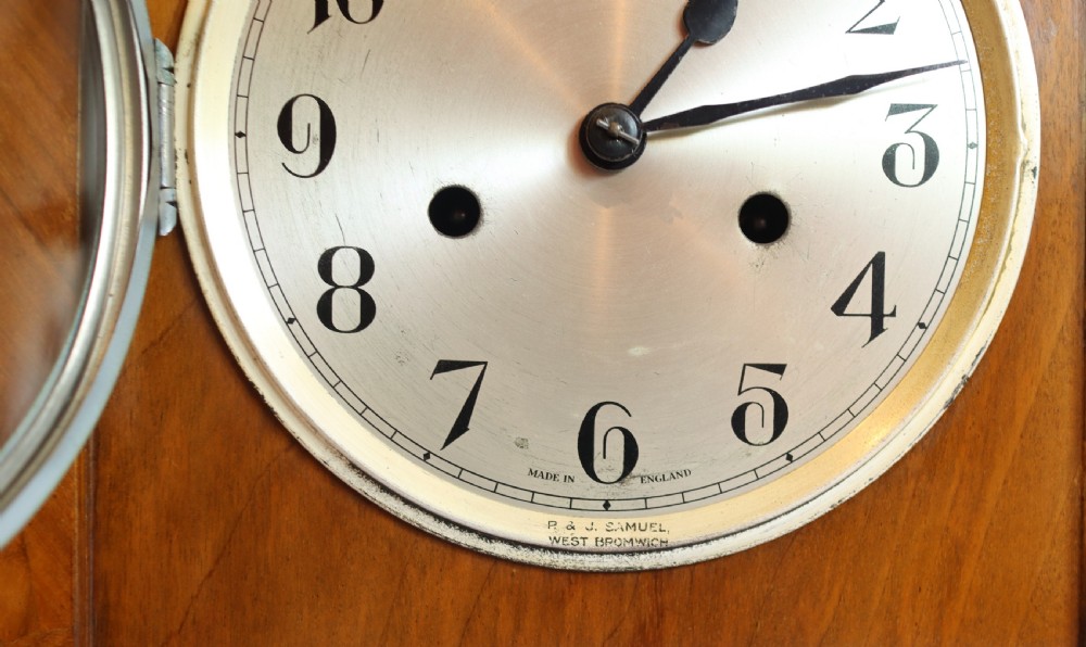 An Art Deco wooden mantel clock featuring an arched case with book-matched veneer and a round silvered dial with Arabic numerals. View VIII