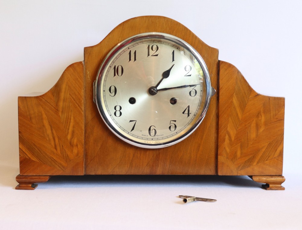 An Art Deco wooden mantel clock featuring an arched case with book-matched veneer and a round silvered dial with Arabic numerals. View IX