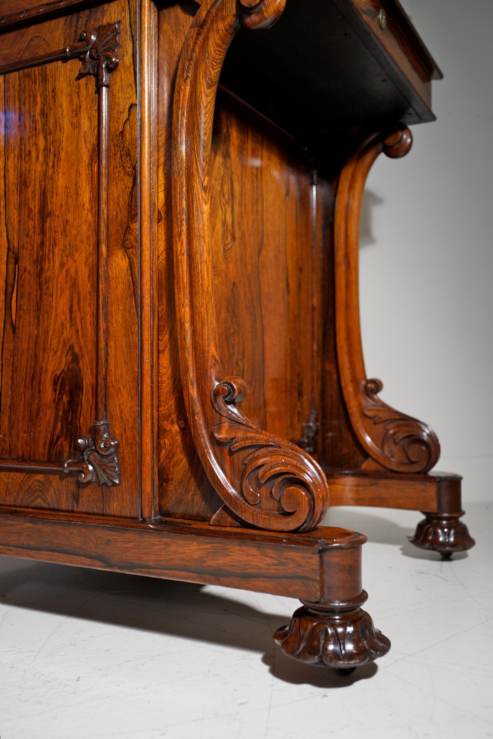 A dark brown rosewood Davenport desk featuring carved scroll front supports, side drawer panelling, and a slanted writing top. View II