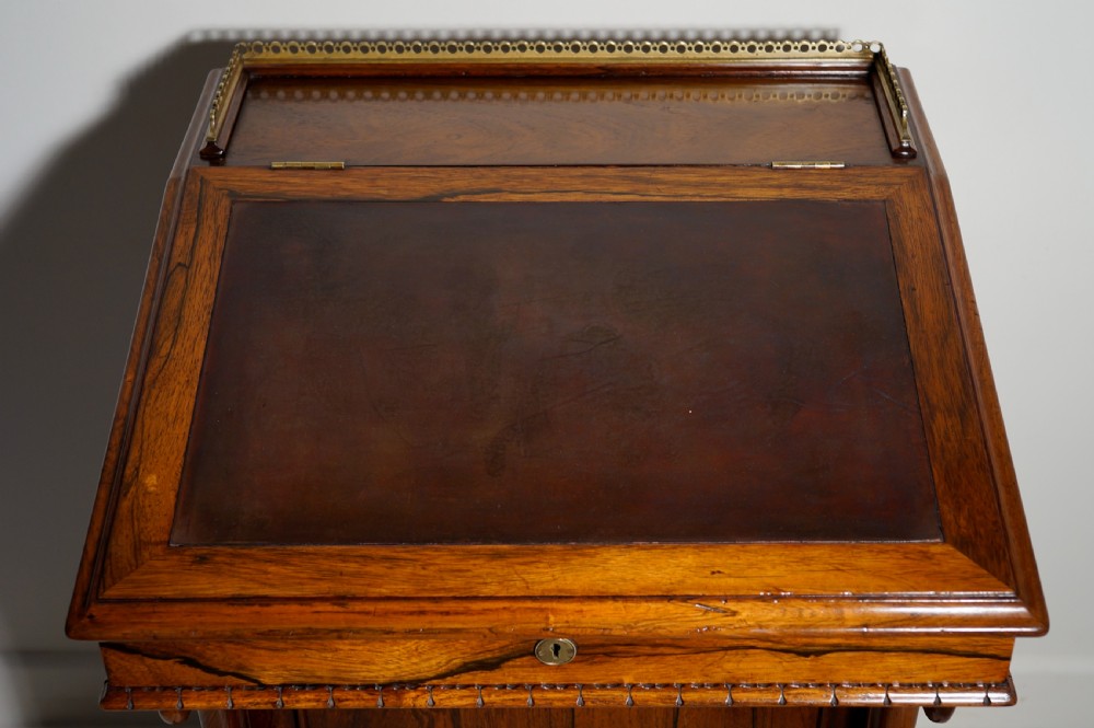 A dark brown rosewood Davenport desk featuring carved scroll front supports, side drawer panelling, and a slanted writing top. View V