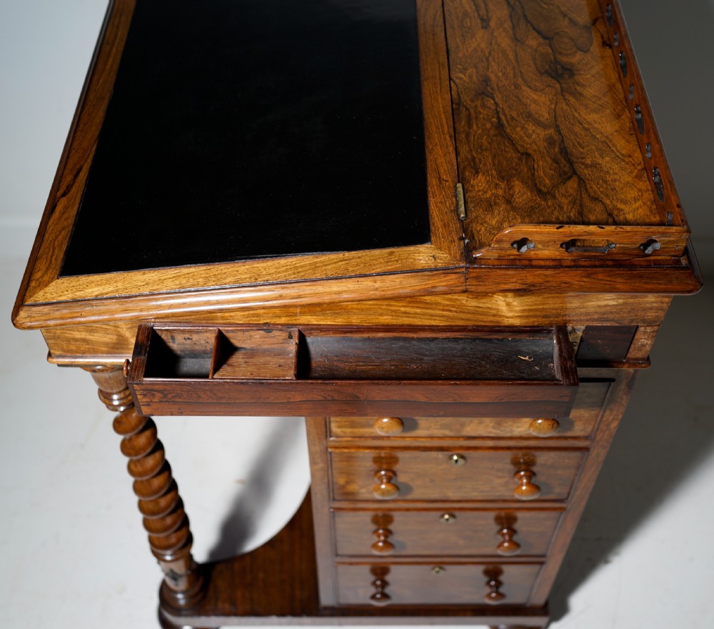 An antique Victorian rosewood Davenport desk featuring a slanted black leather writing surface, a pierced top gallery rail, and turned barley twist front columns. View V