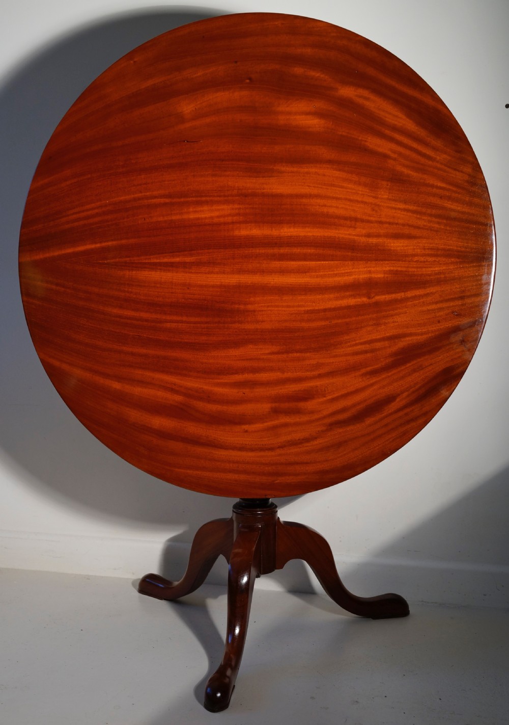 An antique mahogany circular tilt-top table displayed upright on a turned central column and a three-legged tripod base with cabriole legs.
