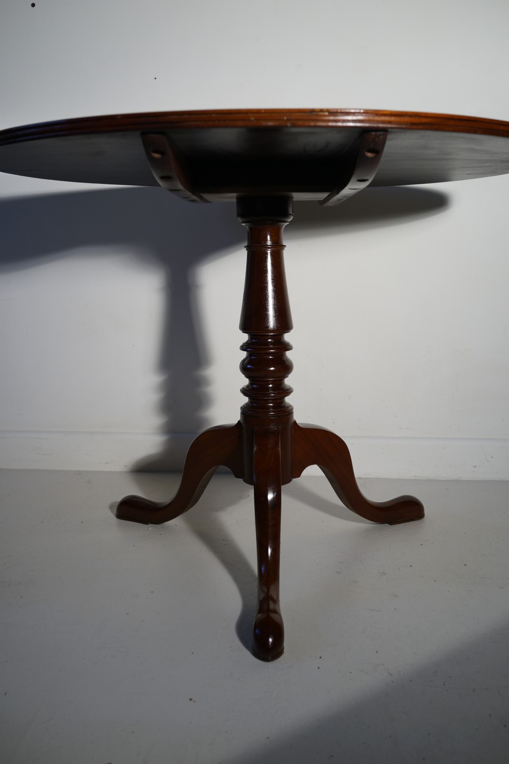 An antique mahogany circular tilt-top table displayed upright on a turned central column and a three-legged tripod base with cabriole legs. View II