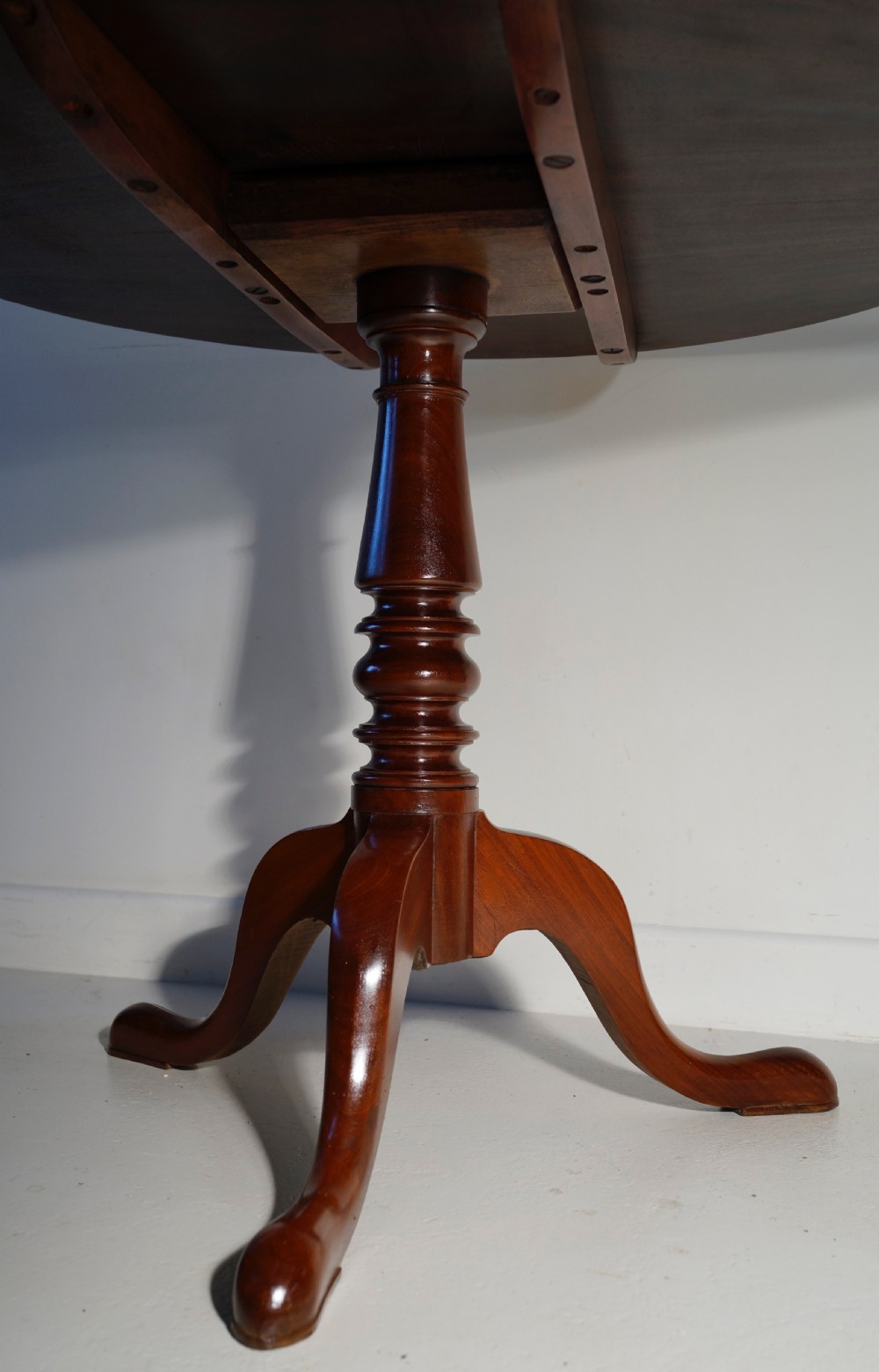 An antique mahogany circular tilt-top table displayed upright on a turned central column and a three-legged tripod base with cabriole legs. View III