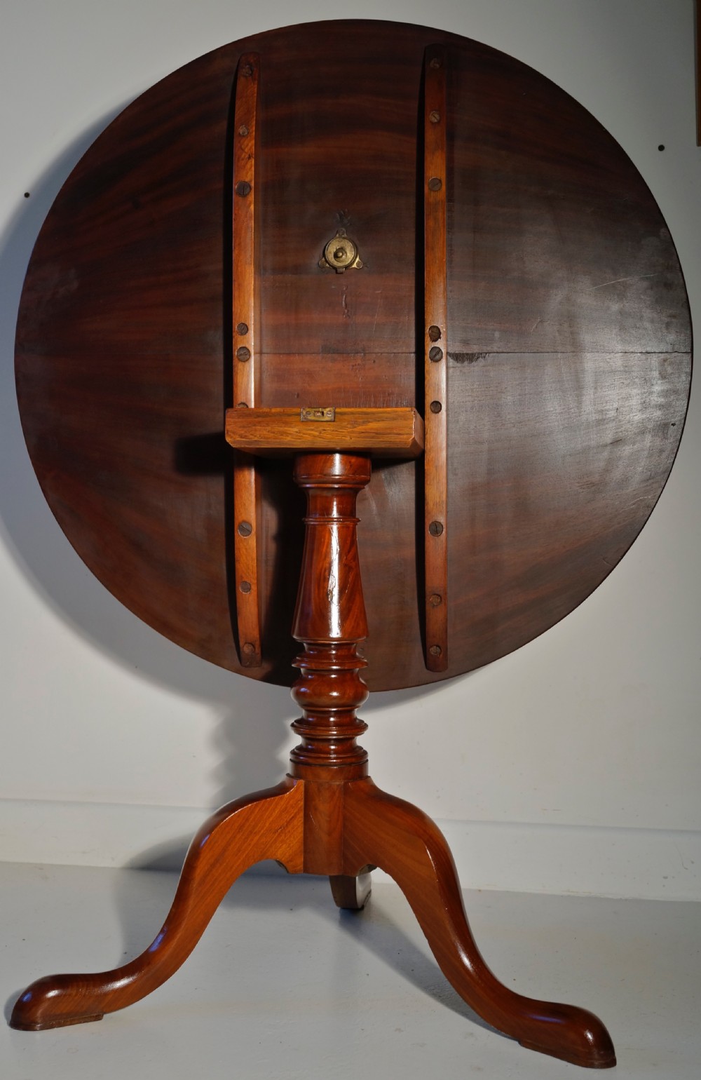 An antique mahogany circular tilt-top table displayed upright on a turned central column and a three-legged tripod base with cabriole legs. View V