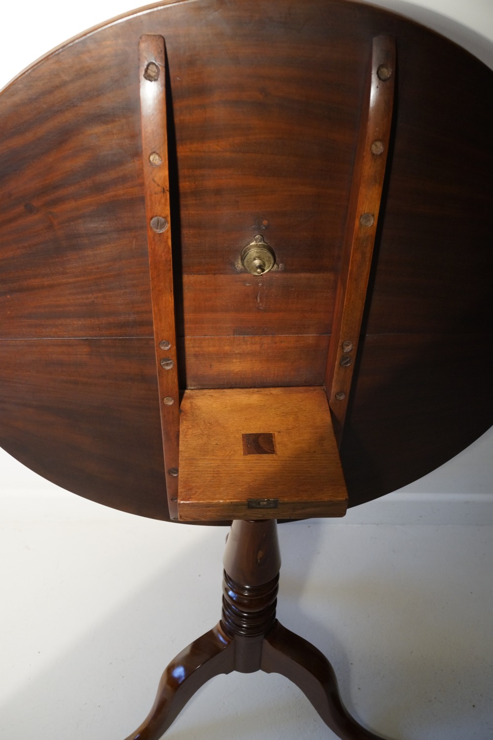 An antique mahogany circular tilt-top table displayed upright on a turned central column and a three-legged tripod base with cabriole legs. View VI