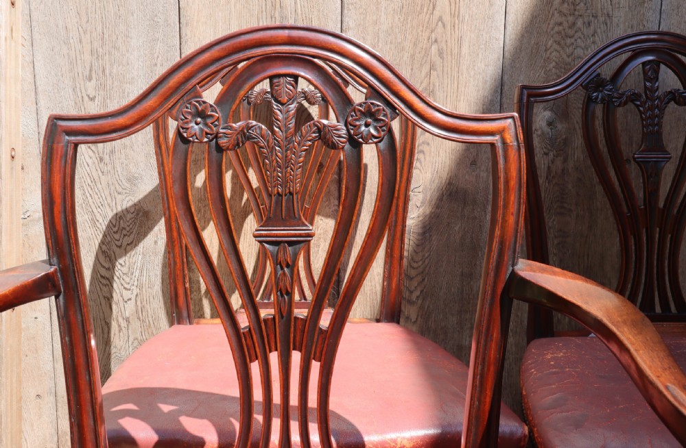 A set of carved mahogany Hepplewhite dining chairs featuring shield-shaped backs, carved wheat splats, and brass-studded red leather seats. View V