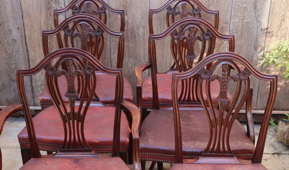 A set of carved mahogany Hepplewhite dining chairs featuring shield-shaped backs, carved wheat splats, and brass-studded red leather seats. View VI