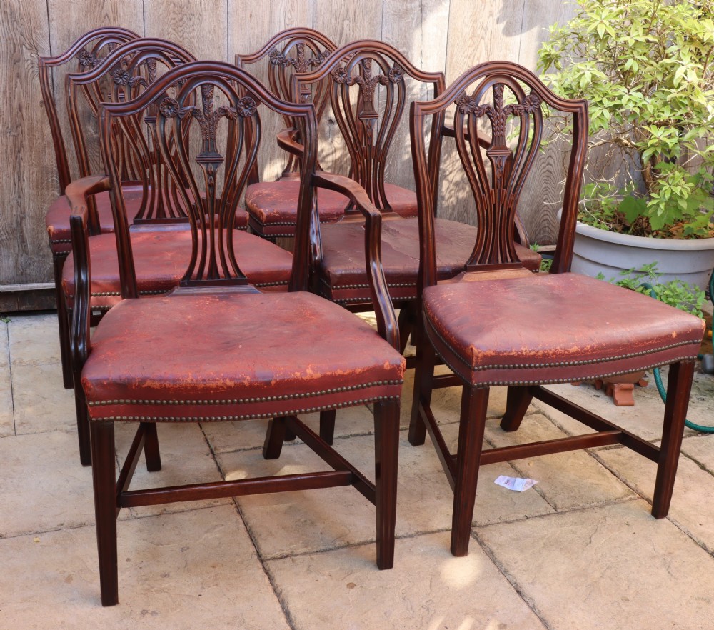A set of carved mahogany Hepplewhite dining chairs featuring shield-shaped backs, carved wheat splats, and brass-studded red leather seats. View VII