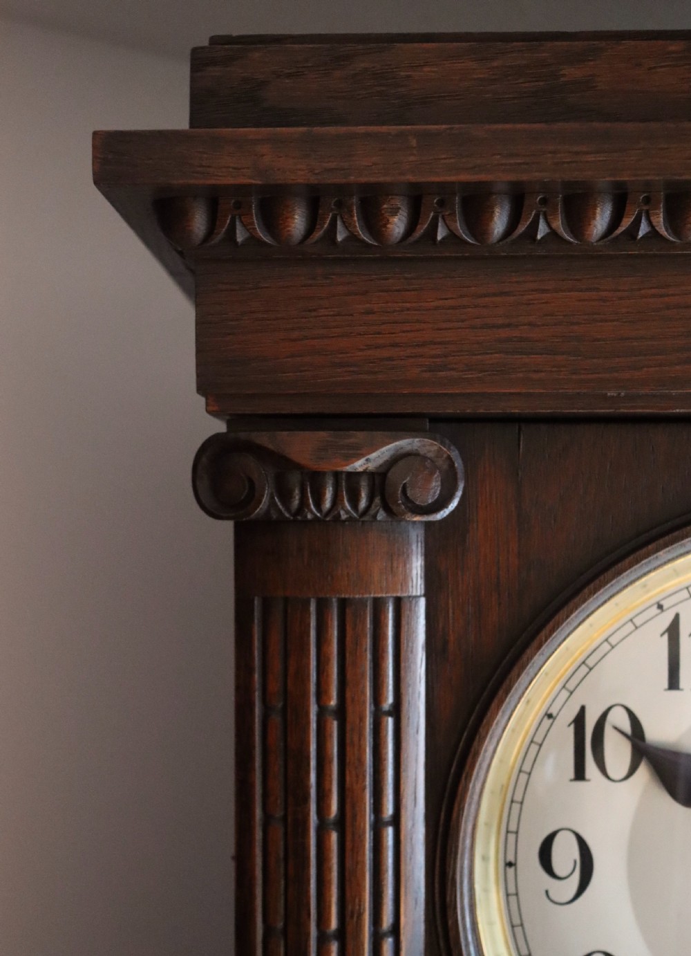 A tall wooden longcase clock featuring fluted corner columns, brass pendulum and weights visible through a glass door, and a circular clock dial with Arabic numerals. View II