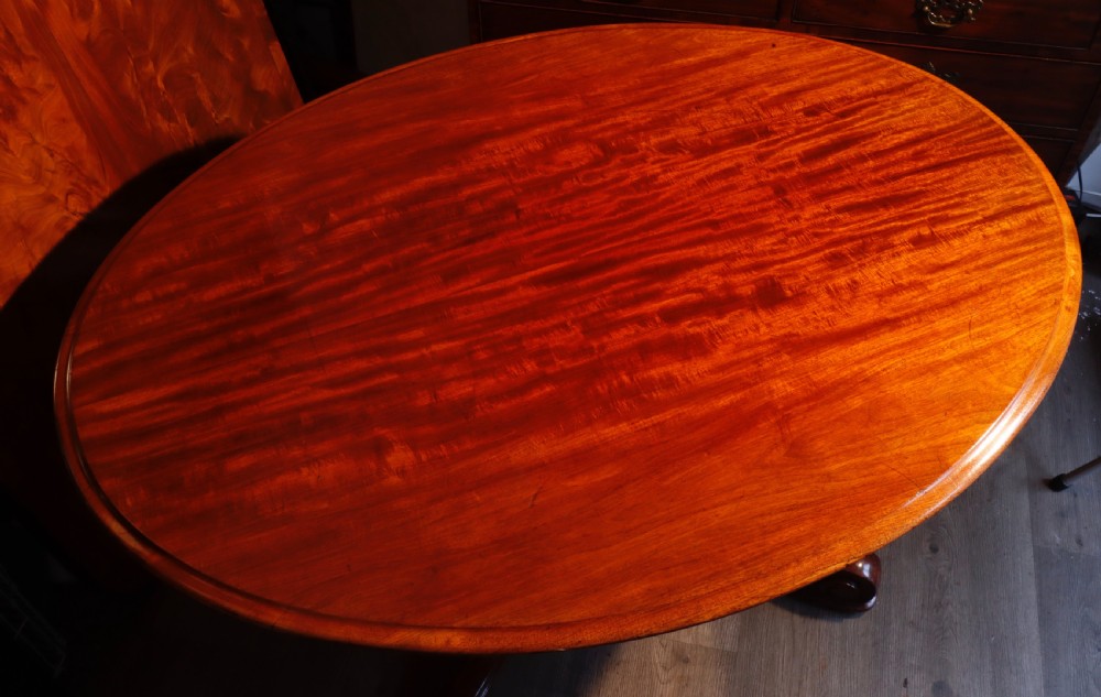 A circular Victorian flame mahogany dining table resting on a turned pedestal with four carved scroll legs. View II