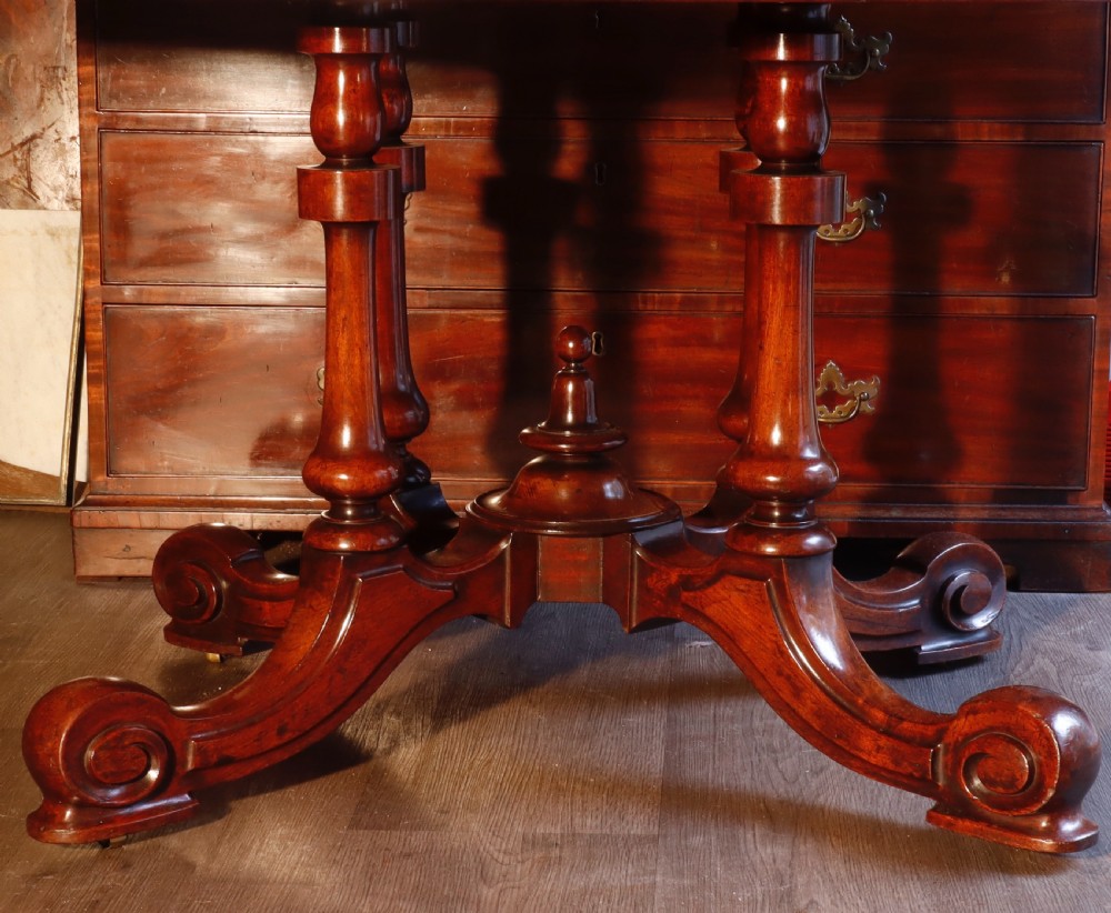 A circular Victorian flame mahogany dining table resting on a turned pedestal with four carved scroll legs. View III