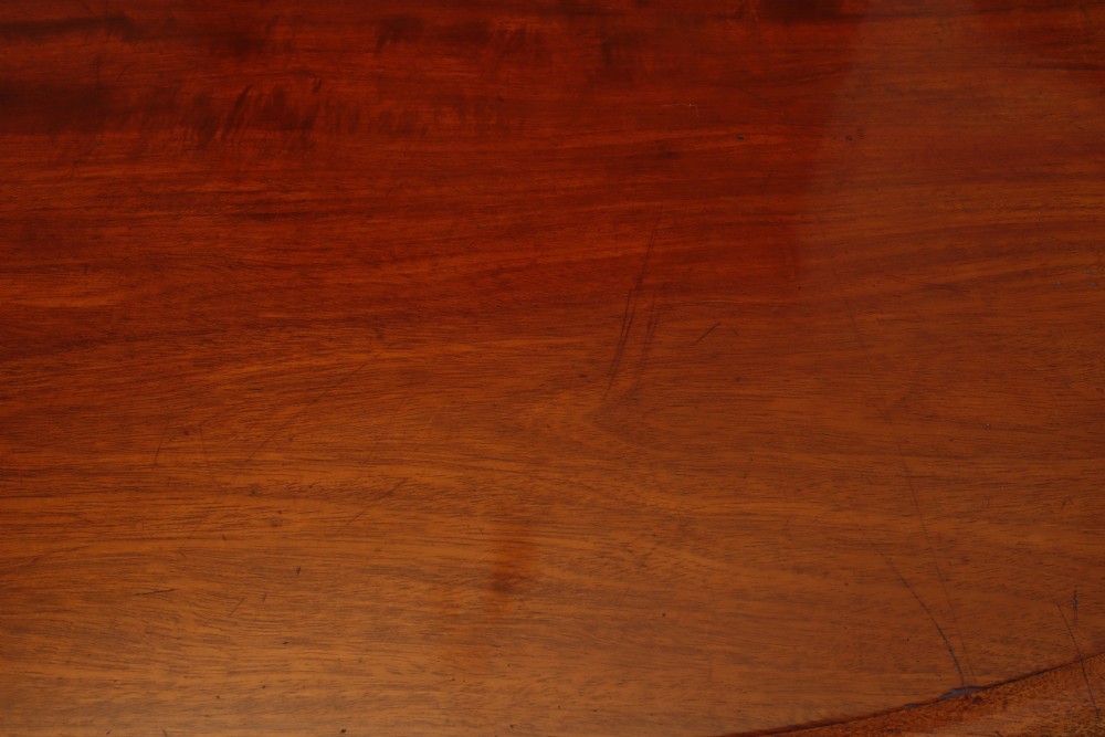 A circular Victorian flame mahogany dining table resting on a turned pedestal with four carved scroll legs. View V